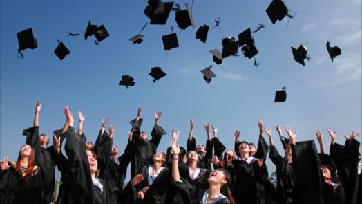 Newly Graduated People Wearing Black Academy Gowns Throwing Hats Up In The Air